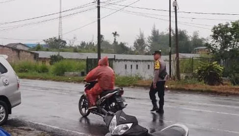 Bhabinkamtibmas Polsek Raya Tetap Bertugas Atur Lalu Lintas di Simpang Sekolah Meski Diguyur Hujan